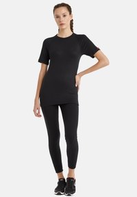 Svart atletisk topp med korta raglanärmar, i kombination med svarta åtsittande leggings. Materialet är slätt och elastiskt. Sneakers har svarta och röda accenter.