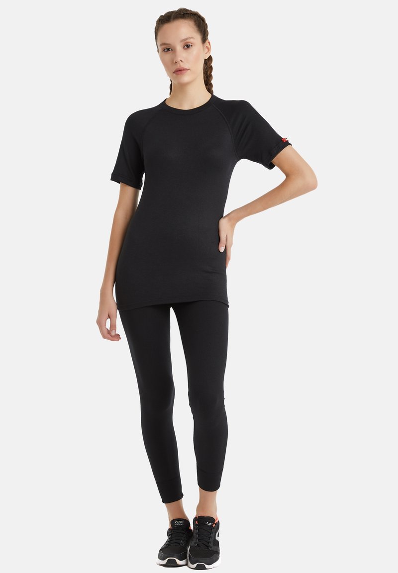 Svart atletisk topp med korta raglanärmar, i kombination med svarta åtsittande leggings. Materialet är slätt och elastiskt. Sneakers har svarta och röda accenter.