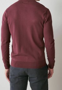 Pull en tricot bourgogne à manches longues, avec un ourlet et des poignets côtelés, présentant une texture lisse et un col rond classique, vu de dos.