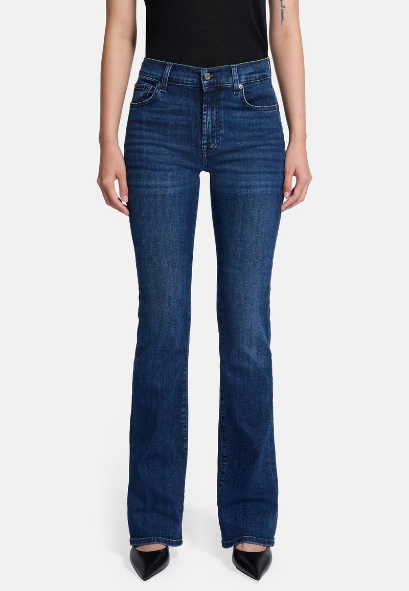 Jeans a zampa d'elefante blu scuro in denim, con tasche frontali e dettagli di sfumatura leggera. Indossati con tacchi a punta neri.