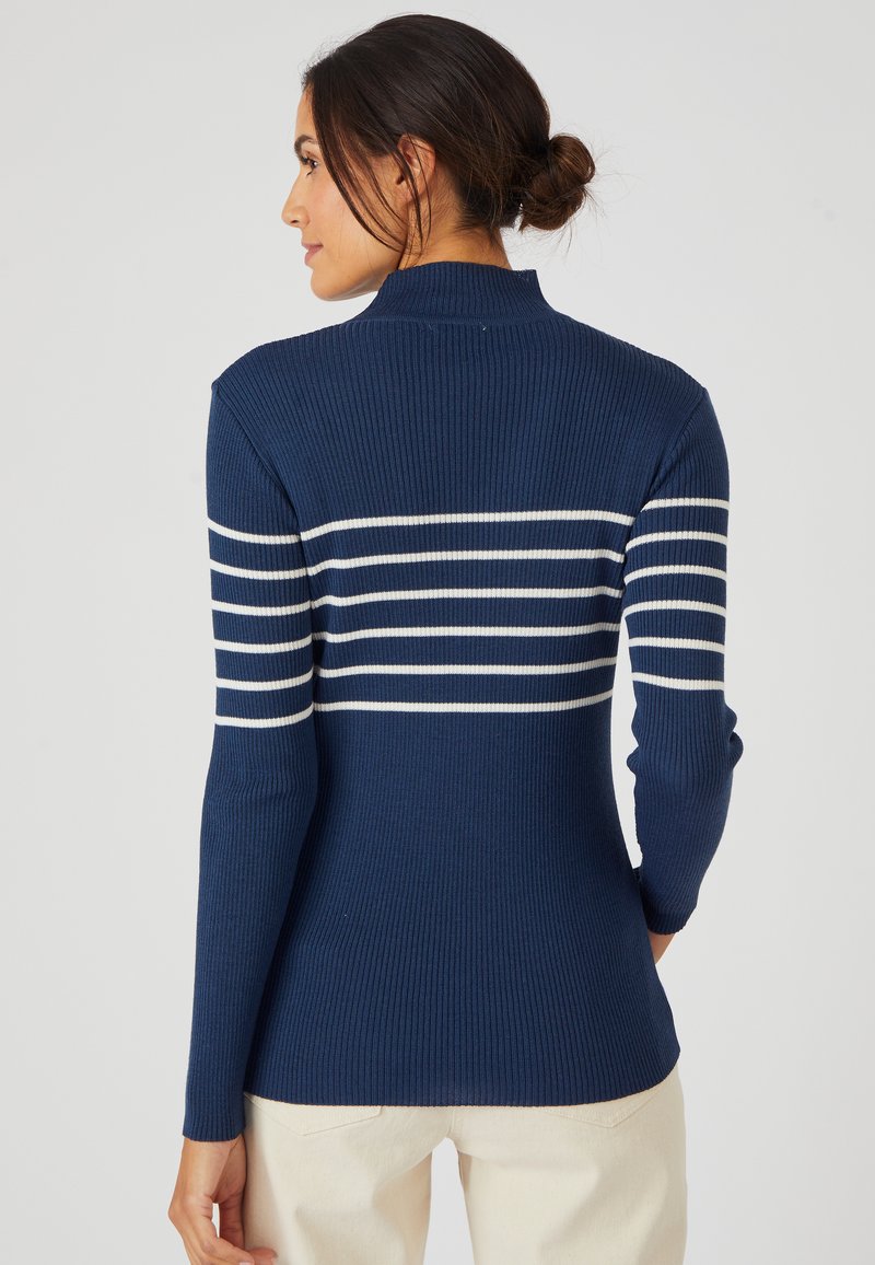 Maglione a coste blu navy con strisce orizzontali bianche sul retro e colletto alto. Il tessuto appare morbido con una silhouette aderente.