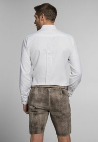 Weißes Langarmhemd mit einer Rückenfalte, kombiniert mit braunen Wildledershorts, die Taschen und sichtbare Nähte aufweisen.
