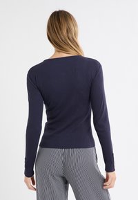 Marineblaues Langarmoberteil in gerippter Struktur mit rundem Ausschnitt und taillierter Passform; kombiniert mit vertikal gestreifter Hose.