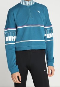 Turbulensfärgad kort sweatshirt med vita och lila ränder, fyrakantig dragkedja och Puma-logotyp på bröstet. Matchad med svarta leggings.