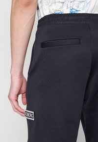 Ciemnoniebieskie dresy wykonane z miękkiego materiału, z elastycznym pasem, bocznymi kieszeniami oraz wyszywaną łatką z logo ICEBERG na nodze.