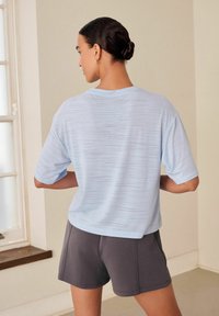 Camicia azzurra a maniche corte con un motivo testurizzato sottile, abbinata a pantaloni corti grigi scuri. Vestibilità rilassata con scollo rotondo.