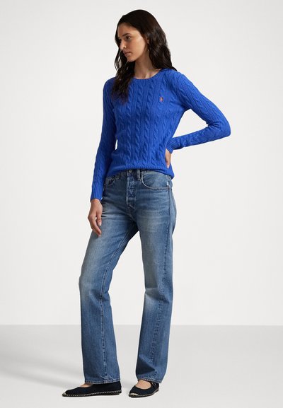 Koboltblå kabelstrikket genser med lange ermer, sammen med lysvaskede jeans og svarte leiligheter med dekorativ kant.