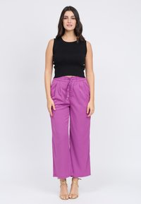 Top negro sin mangas, textura acanalada. Pantalones de pierna ancha rosa con cintura ajustable. Acentos de hardware dorado y tacones nude con tiras.