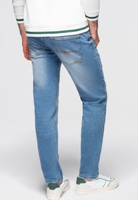 Jeans en denim bleu clair avec une coupe droite, une décoloration subtile et deux poches arrière. Portés avec des baskets blanches et vertes.