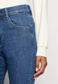 Jeans i medelblå tvätt med rak modell, femficksdesign och kontrasterande sömmar. Kombineras med en krämfärgad ärm.