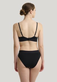 Completo bikini nero con spalline regolabili, chiusura a gancio sulla parte superiore e pantaloni a vita alta. Tessuto liscio ed elasticizzato con dettagli minimi.