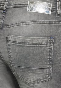 Vaqueros de denim gris con una etiqueta de herrajes plateada, bolsillo trasero con costura recta y una textura ligeramente deslavada.