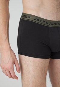 Schwarze Boxershorts mit einem dunkelgrünen Gummibund, auf dem "JACK & JONES" in schwarzer Schrift steht. Glattes Material, enganliegendes Design, sichtbare Nähte.
