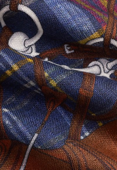 Κοντινό πλάνο υφασμάτινης υφής με μπλε φόντο και μοτίβο από καφέ λουριά, λευκές αγκράφες και κίτρινες λεπτομέρειες.