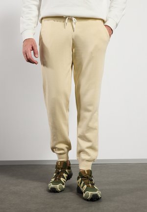 Beige sweatpants with a drawstring waistband and side pockets, paired with green and beige camo sneakers featuring a sturdy sole and laces.