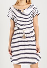 Robe rayée en crème et bleu marine, avec un col rond et une ouverture en forme de clé, des manches courtes, une taille élastique avec cordon de serrage, et des pompons décoratifs.