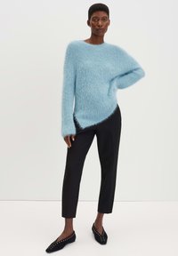 Hellblauer, flauschiger Pullover mit asymmetrischem Saum, kombiniert mit enganliegenden schwarzen Hosen und schwarzen, studs-dekorierten Ballerinas. Glatte Textur, lässiges Design.