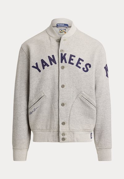 Ανοιχτό γκρι φούτερ με κουμπιά και "YANKEES" με σκούρα μπλε γράμματα στο στήθος και λογότυπο των New York Yankees στο μανίκι.