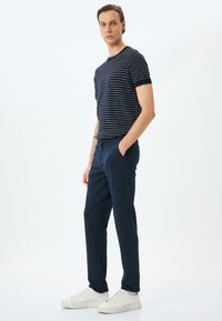 Marine gestreepte T-shirt met korte mouwen gecombineerd met marineblauwe broek en witte sneakers. De stof lijkt glad te zijn met een casual pasvorm en zakken in de broek.