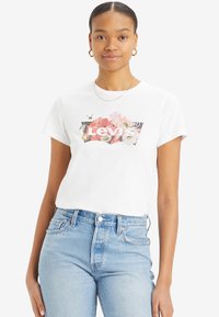 Vit bomullströja med ett blommönster och "Levi's" logotyp i fet stil. Parat med ljusblå denimjeans. Korta ärmar.