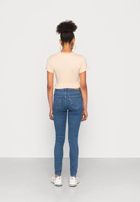 T-shirt beige de mangas curtas com riscas leves, combinado com jeans skinny azuis de cintura alta. Apresenta uma etiqueta de marca e bolsos traseiros.
