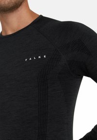 Zwarte langwerpige shirt met textuurgebreide patronen en een aansluitend ontwerp. Voorzien van het FALKE-logo in het grijs op de borst.