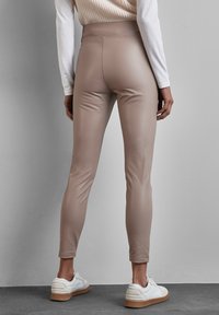 Beige faux leren leggings met een hoge taille, slanke pasvorm en een soepele textuur, gecombineerd met witte sneakers met een lichte zool.