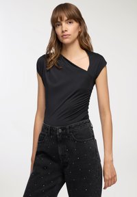 Body nero aderente con maniche corte e scollatura profonda, abbinato a jeans neri a vita alta decorati con strass sparsi.
