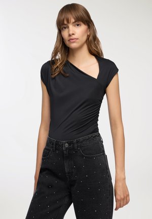 Body nero aderente con maniche corte e scollatura profonda, abbinato a jeans neri a vita alta decorati con strass sparsi.