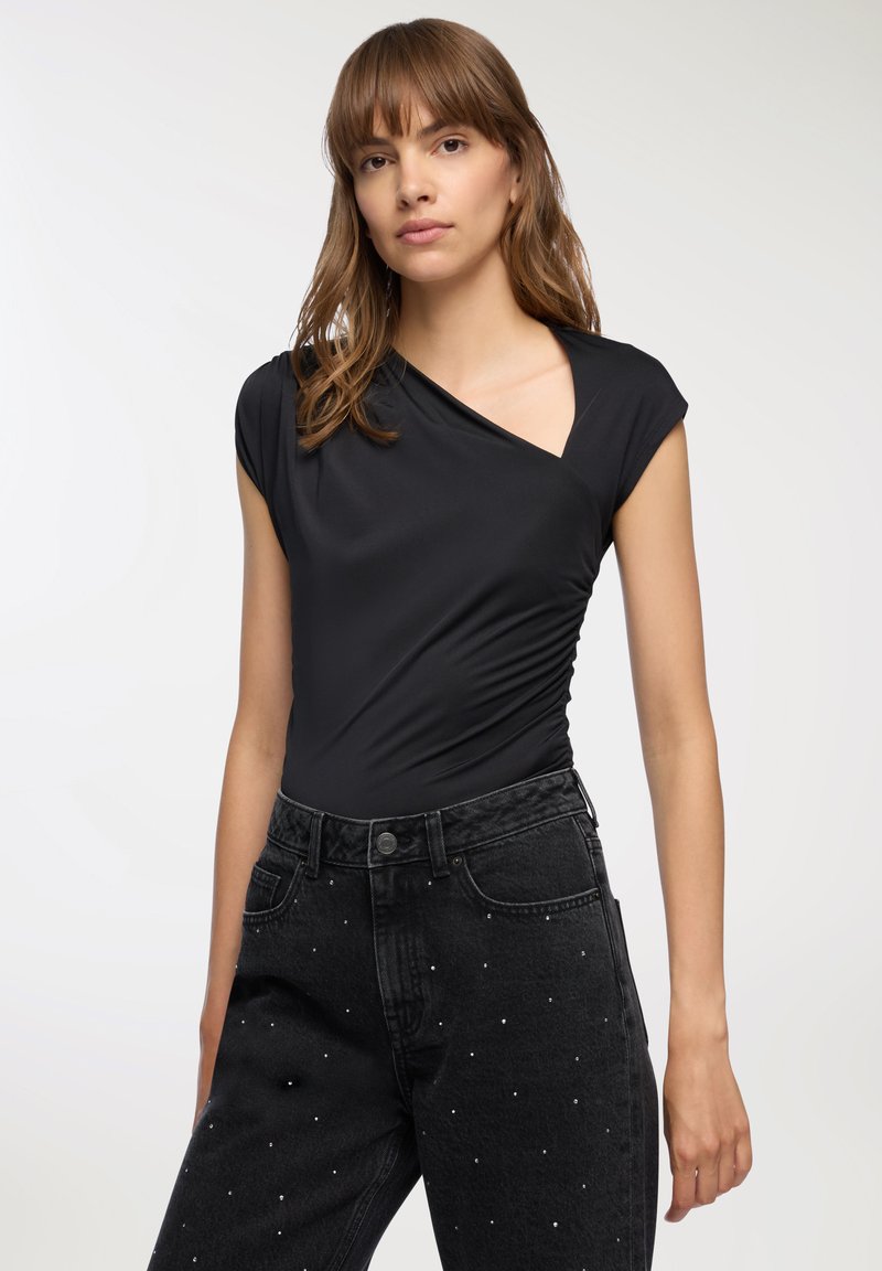 Body nero aderente con maniche corte e scollatura profonda, abbinato a jeans neri a vita alta decorati con strass sparsi.