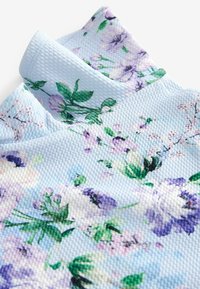 Stoff mit floralem Muster in Hellblau, mit strukturiertem Gewebe, das grüne Blätter und lila Blumen zeigt. Auffällig durch seine lebendigen Farben und das detaillierte Design.