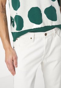 White cotton jeans paired with a green and white polka dot knit top. The top features a round hem and ribbed accents.