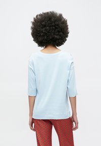 Jasnoniebieska bawełniana bluzka z rękawami do łokcia, okrągłym dekoltem i prostym wzorem, zestawiona z czerwonymi legginsami w diamentowe wzory.