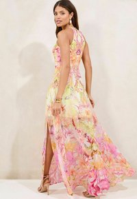 Abito lungo floreale in giallo pastello e rosa con uno spacco laterale, realizzato in tessuto trasparente. Presenta motivi di farfalle e fiori, design senza maniche.