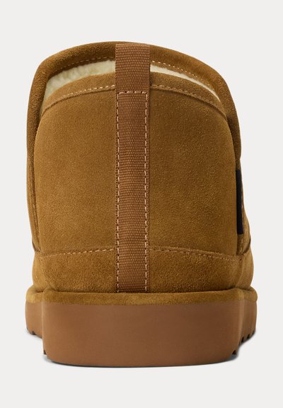 Brun semsket tøffel med mykt fôr, med en kontrasterende teksturert stropp bak og en flat gummisåle.