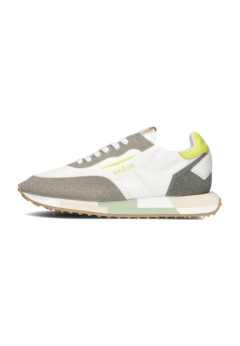 Basket de sport avec un upper en cuir blanc, des accents en paillettes grises, un talon vert et une semelle texturée avec des détails en caoutchouc gomme.
