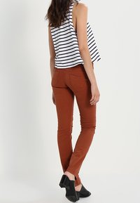 Ruskohi väri, kapea malli puuvillasekoitekankaita, joissa on takataskut, yhdistetty musta-valkoisiin raidallisiin hihattomiin toppeihin. Mustat kengät.