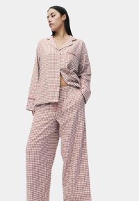 Ensemble de pyjama à carreaux roses et blancs, comprenant une chemise à boutons et un pantalon à taille élastique, avec une coupe décontractée et une texture de tissu douce.