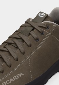 Καφέ σουέντ αθλητικό παπούτσι με κορδόνια ελιάς πράσινου χρώματος, λευκό ράψιμο και υφασμάτινη θηλιά με λευκό λογότυπο στη γλώσσα.