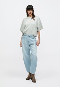 T-shirt gris clair oversize associée à un jean taille haute bleu clair à jambes droites, complétée par des bottines marron.