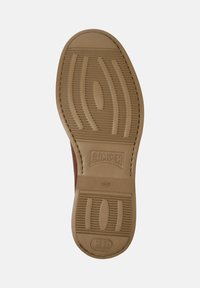 Suola di una scarpa Camper marrone che mostra la gomma testurizzata con il logo del marchio e l'impronta della taglia, evidenziando la presa e i dettagli di design.