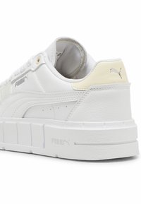 Sneaker bianca in pelle con finitura testurizzata, dotata di suola spessa, dettagli dorati e logo Puma sul lato e sul tallone.