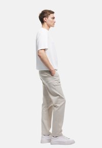 Witte gestructureerde kortge mouw shirt, beige rechte broek en witte schoenen. Zijaanzicht toont de relaxte pasvorm en neutrale kleuren.