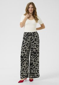 Pantalons larges noirs à motif floral blanc, avec taille élastique et cordon de serrage. Associés à un haut blanc ajusté et des talons rouges.