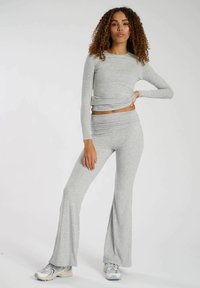 Haut gris à manches longues avec détail torsadé et pantalon évasé assorti ; tissu doux et extensible avec une texture lisse. Chaussures de sport décontractées.