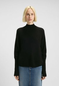 Schwarzer, gestrickter Pullover mit hohem Kragen und langen Ärmeln, der eine weiche Textur und eine lockere Passform bietet, kombiniert mit einem blauen Denim-Rock.