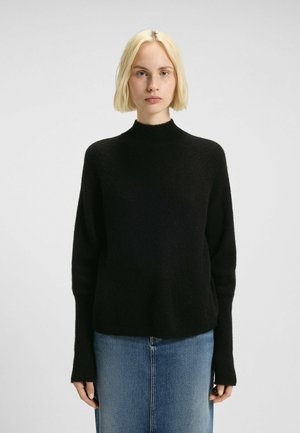 Zwarte gebreide trui met hoge hals en lange mouwen, met een zachte textuur en een relaxte fit, gecombineerd met een blauwe denimrok.