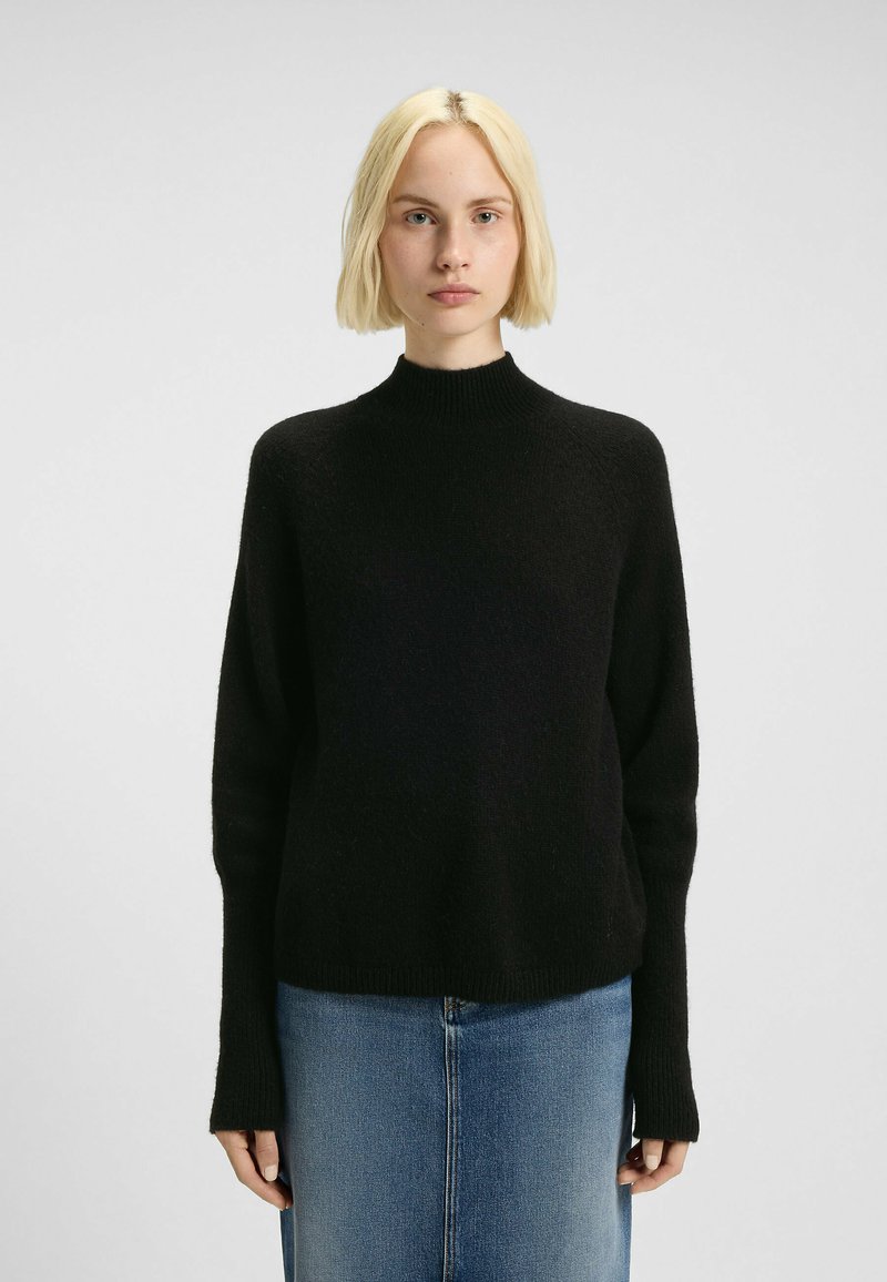 Schwarzer, gestrickter Pullover mit hohem Kragen und langen Ärmeln, der eine weiche Textur und eine lockere Passform bietet, kombiniert mit einem blauen Denim-Rock.