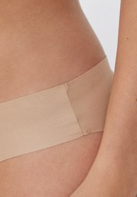 Beige nahtloses Stoffband mit gerippter Textur, teilweise über der Haut sichtbar, zeigt glatte Kanten und minimalistisches Design.