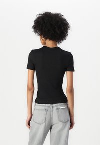 Top nero fitted a maniche corte con texture a costine, abbinato a jeans grigio chiaro a vita alta con tasche posteriori e una vestibilità comoda.